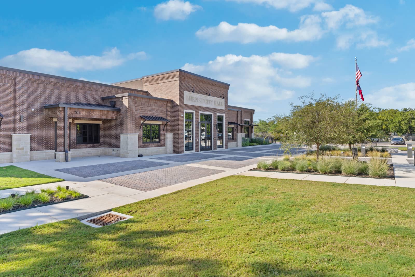 An angled view of Burnet City Hall framed by trees, native planting and lawn