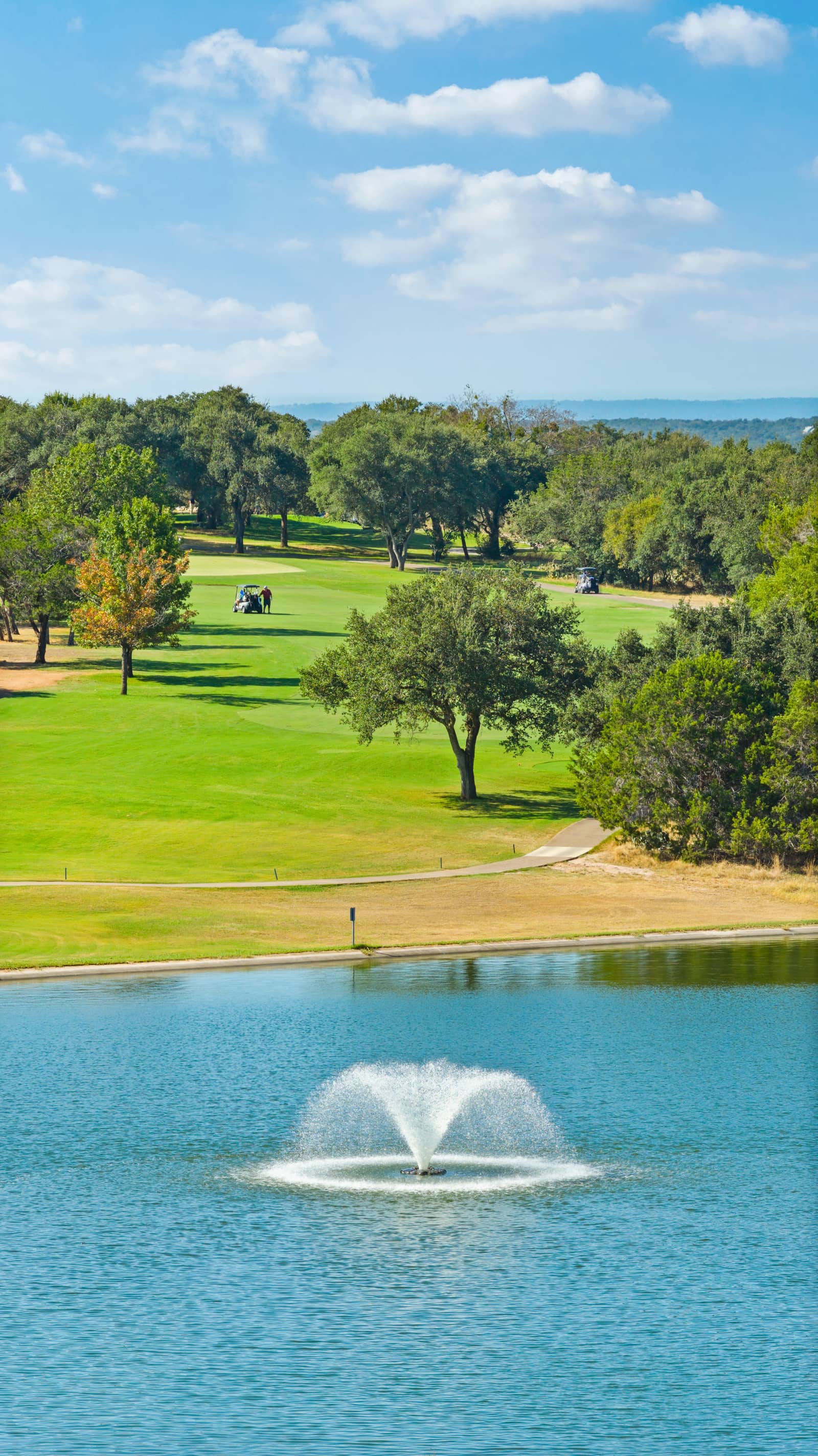 A fountain in the pond below the fairway and oak trees at Delaware Springs Golf Course
