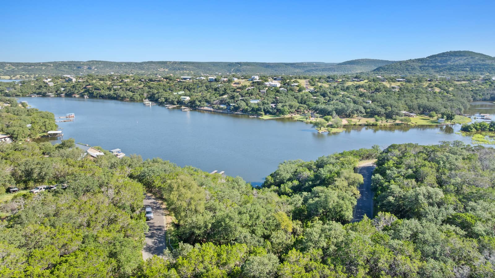 Aerial view across Inks Lake toward a wooded shoreline and Hill Country hills
