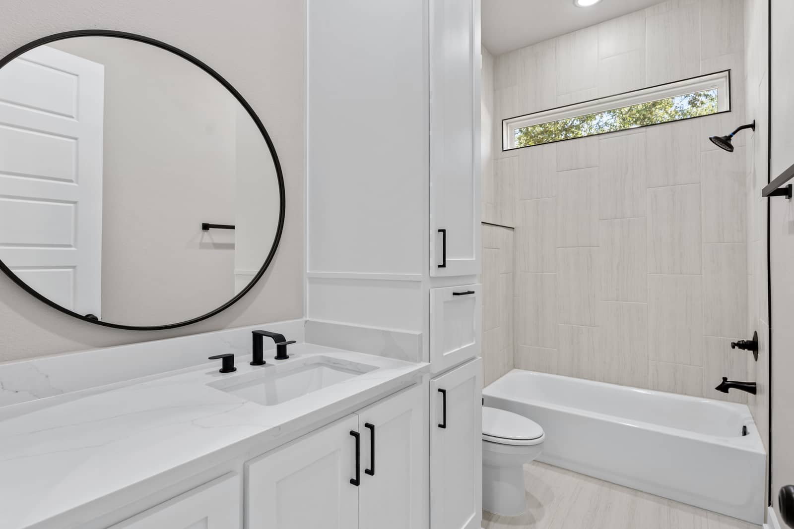 Guest bathroom with a white vanity, round mirror and tiled tub surround at 265 Sunday Drive